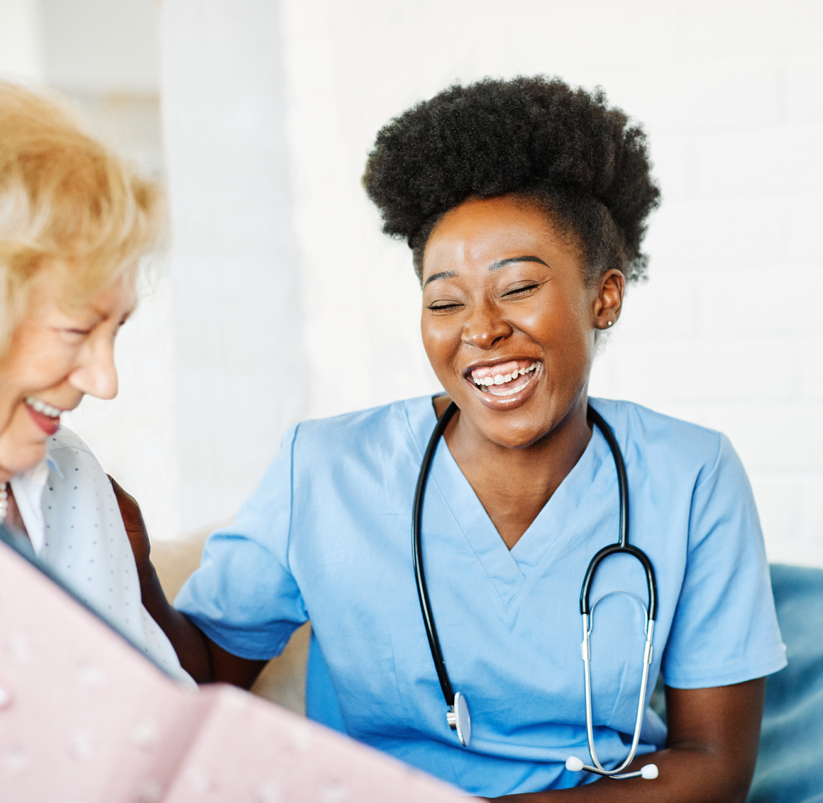 Respite Care Smiling nurse in blue scrubs shares a lighthearted moment with an elderly woman.