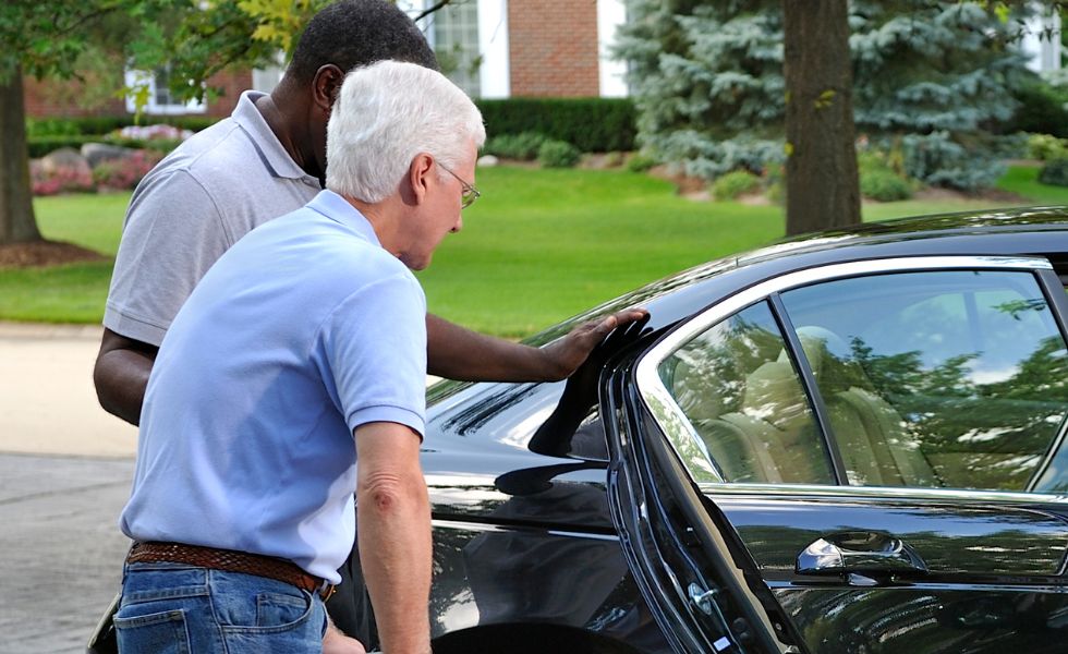 Caregiver assisting senior man into a car in a residential neighborhood