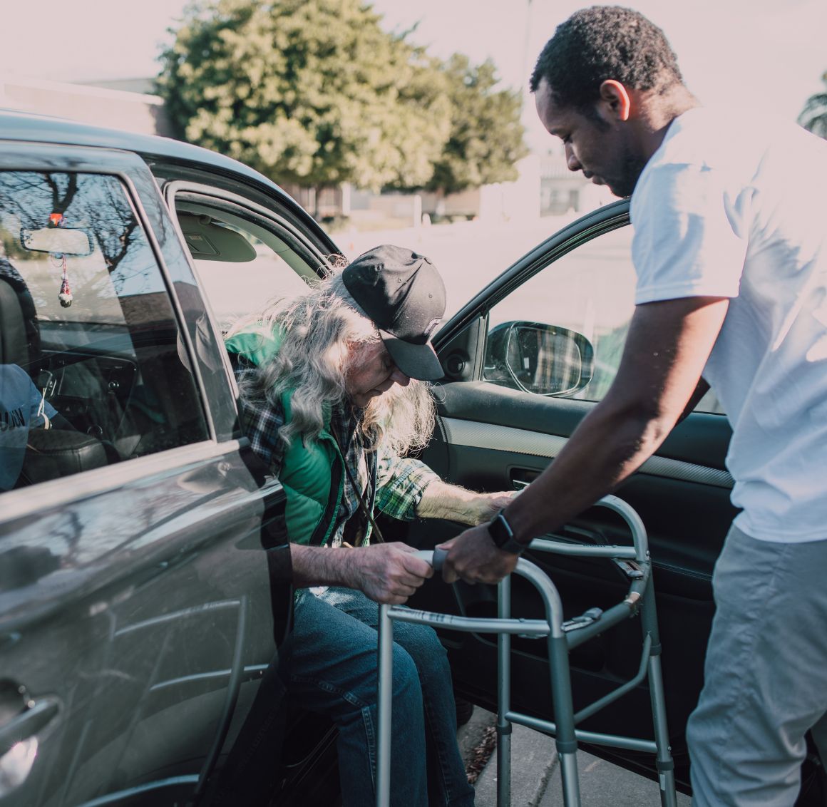 Transportation Caregiver assisting elderly man with walker out of a car