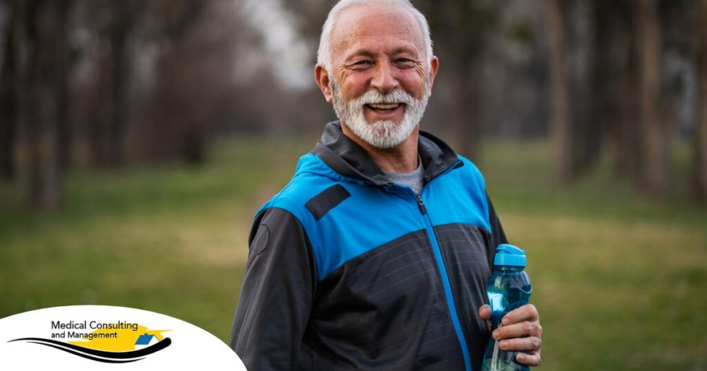 An older man smiles with a water bottle while exercising, representing the benefits of encouraging exercise when caring for seniors at home.