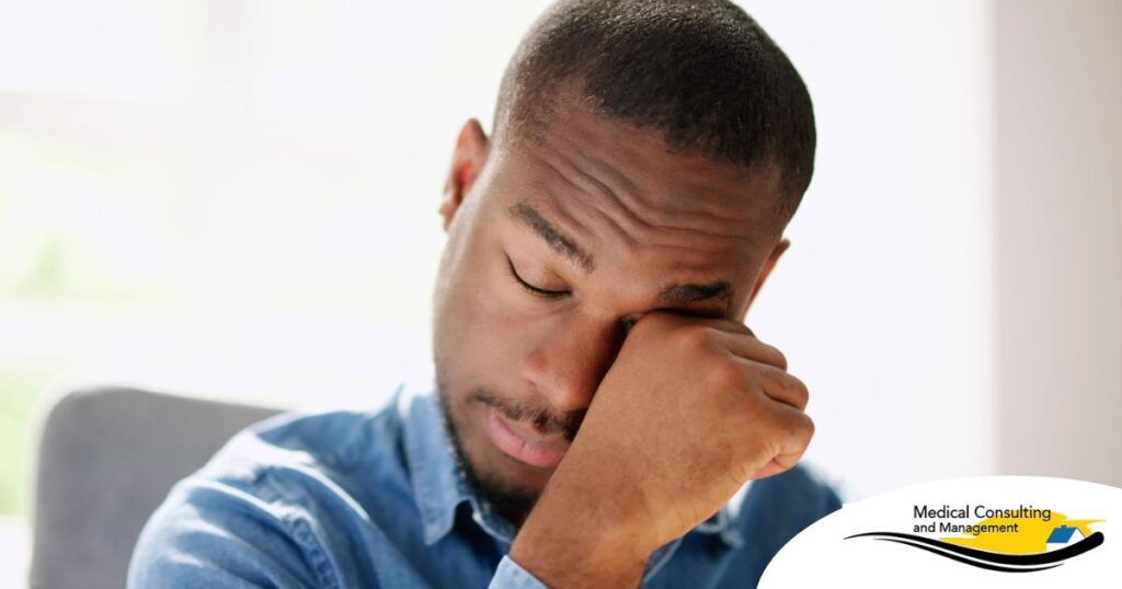 A man tiredly rubs his eyes, representing the exhaustion that can come with family caregiving.