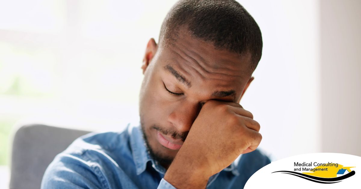 A man tiredly rubs his eyes, representing the exhaustion that can come with family caregiving.
